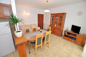 A dining area with a table, chairs, a potted plant, a cabinet, and a television. - Apartments Grozdana (Postira)