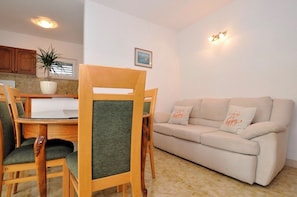 A dining area with a wooden table and chairs, a beige sofa, a potted plant, and a framed picture on the wall. - Apartments Grozdana (Postira)