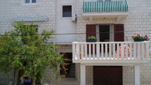 A two-story building with a balcony, a small window, and a door. - Apartments Grozdana (Postira)