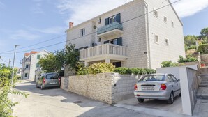 Un edificio de dos plantas con un balcón, un muro de piedra y coches estacionados.