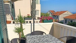 A balcony with a table and chairs, a potted plant, and a view of neighboring houses. - Apartments Grozdana (Postira)