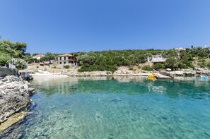 A clear coastal water body with rocky shores, surrounded by residential buildings with red roofs and greenery.