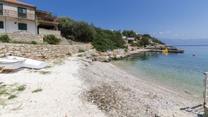 A coastal property with a stone staircase leading to a building with green shutters, a clear view of the sea, and a small boat on the shore. - Apartments Davorka (Gdinj)