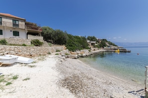 A coastal building with a stone staircase leading to a balcony, a clear view of the sea, and a small boat on the shore. - Apartments Davorka (Jelsa)
