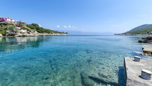 A clear coastal view with a rocky shoreline, a pier, and buildings on the left. - Apartments Davorka (Gdinj)