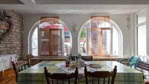 A dining area with a table set for four, two large arched windows, a brick wall, and a wooden bench. - Apartments Davorka (Gdinj)