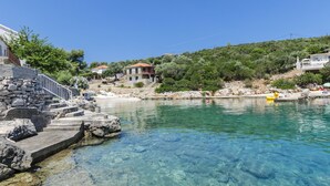 A clear blue pool surrounded by stone steps and a stone wall, with houses in the background. - Apartments Davorka (Gdinj)