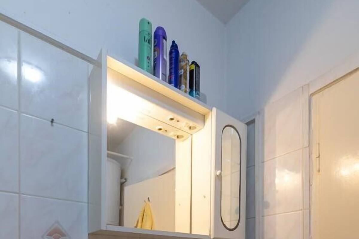 Un baño con un lavamanos blanco, un espejo y un estante sobre el espejo con artículos de aseo.