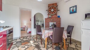 Μια κουζίνα με δάπεδο από πέτρινα πλακάκια, έναν τοίχο από τούβλα και μια τραπεζαρία με τέσσερις καρέκλες και ένα τραπέζι.