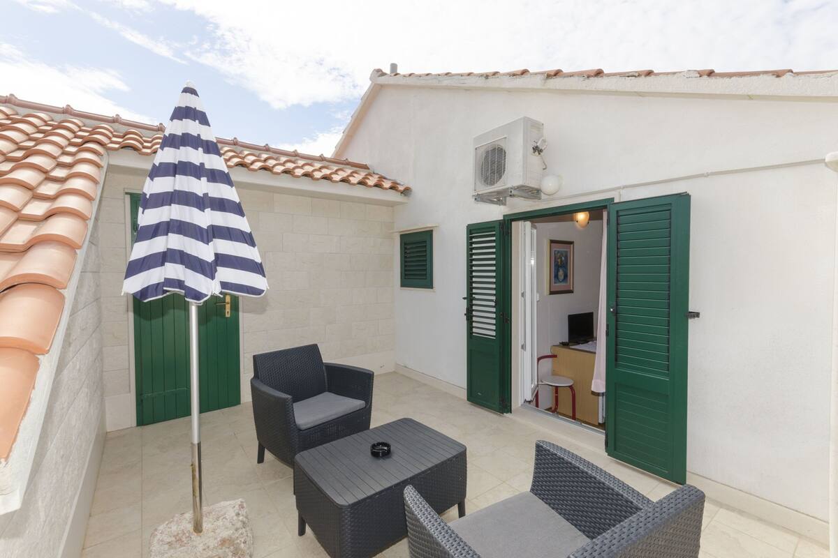 An outdoor patio with wicker furniture, a striped umbrella, and a tiled roof.