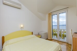 A bedroom with a bed, a nightstand, a small bedside table, an air conditioner, a sliding glass door to a balcony with outdoor furniture, and a view of the sea. - Apartment and Rooms Mate (Bol)