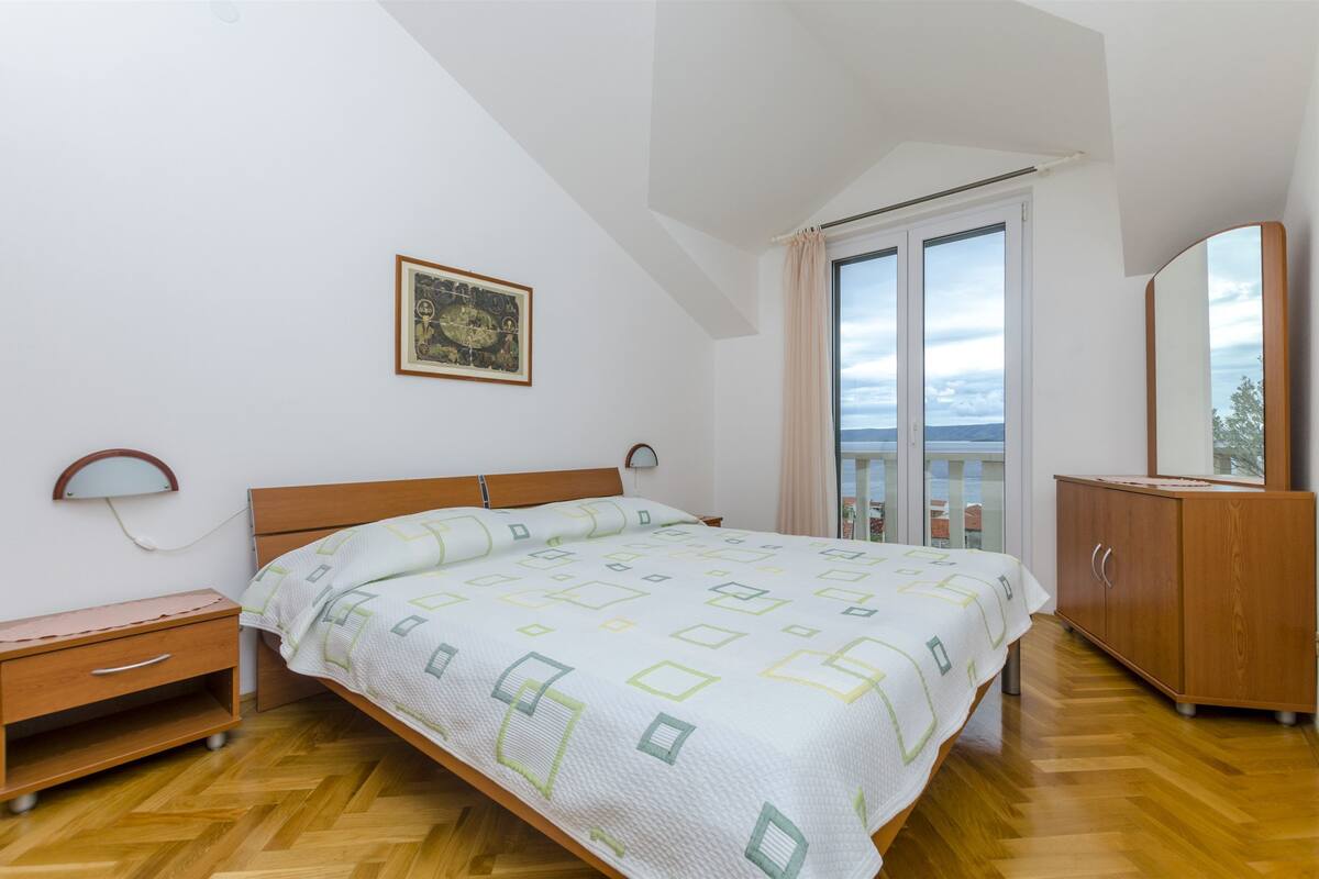 A bedroom with a bed, wooden nightstand, dresser, and a large window with curtains.