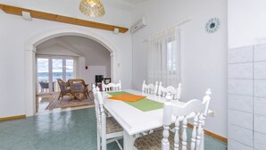 Un comedor con una mesa y sillas blancas, un mantel individual verde, y vistas al exterior a través de un arco.