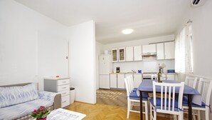 A compact living space with a kitchenette, a dining area with a table and chairs, a sofa, and a small side table with a potted plant. - Apartment Danica (Makarska)