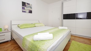 A neatly arranged bedroom with a bed, a nightstand, a lamp, and a green rug. - Apartment Danica (Makarska)