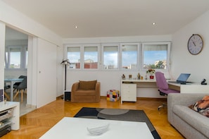 Enjoy a city view from the large window in this apartment's spacious living area, featuring a comfortable sofa and desk workspace.