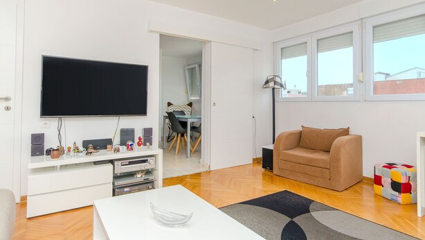 A modern living room with a flat-screen TV, a sofa, a coffee table, and a dining area visible through an open door. - Apartment Sunny (Split)