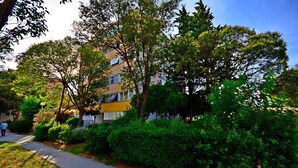 A residential building with a yellow facade, surrounded by lush greenery and a sidewalk. - Apartment Sunny (Split)