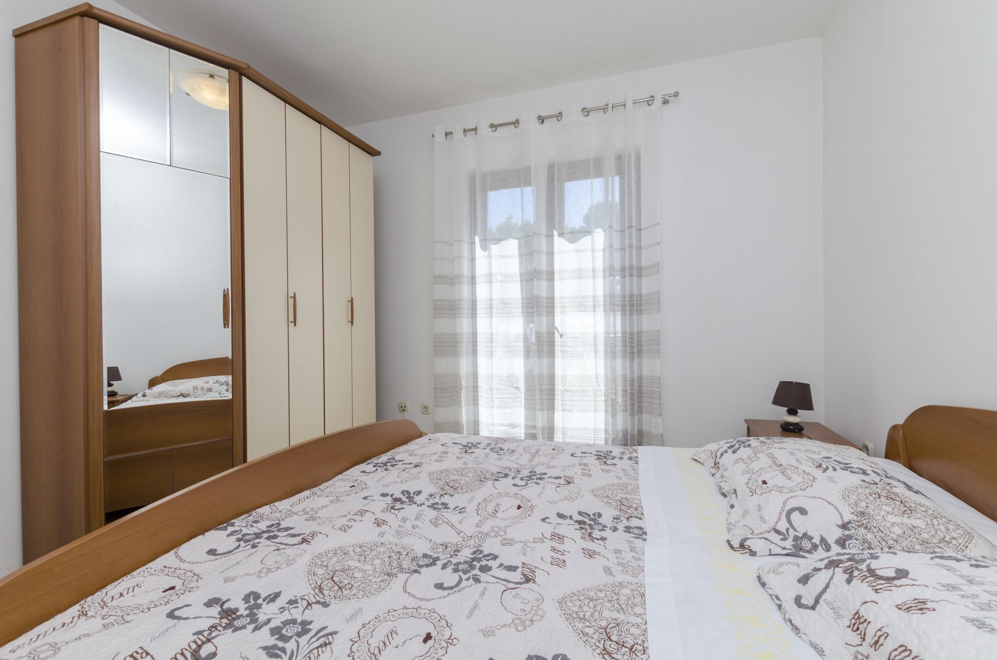 Une chambre à coucher comprenant un lit, une armoire, une table de chevet et une fenêtre avec des rideaux.