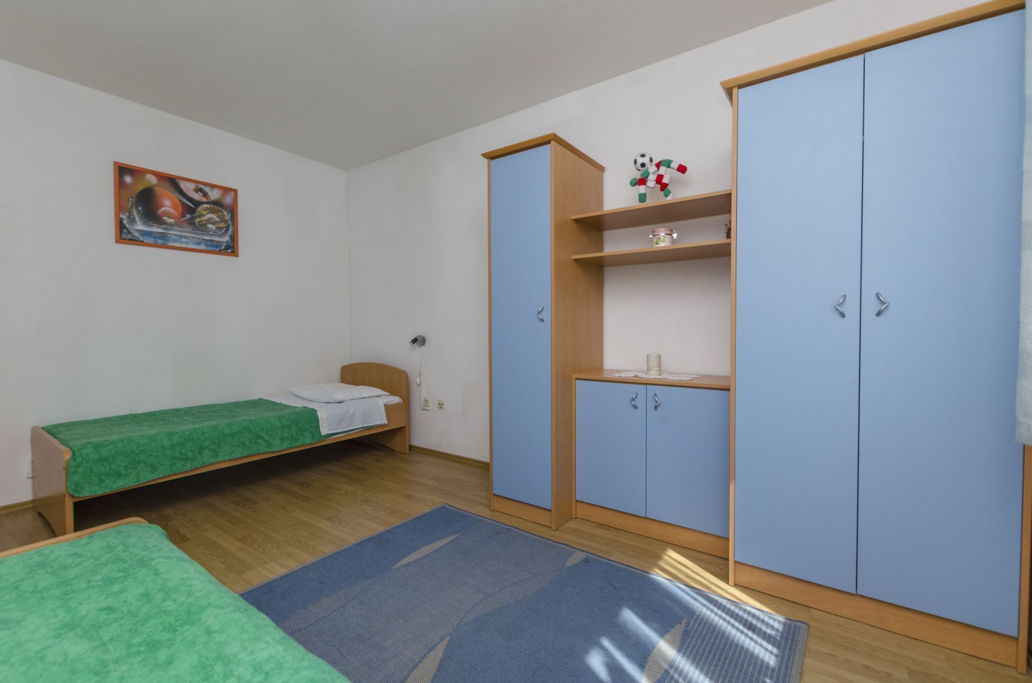 Een kamer met een bed, een bureau, een kledingkast en een schilderij aan de muur.