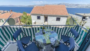 Un balcón con mesa y sillas, con vista a un pueblo costero de edificios con tejados de tejas y vistas al mar.