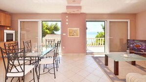 A spacious living area with a glass dining table and chairs, a sofa, and a TV. There is a balcony with a view of the sea. - House Ivan (Mimice)