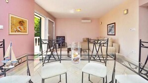 A dining area with a glass table surrounded by chairs, a glass vase with flowers, and a sofa in the background. - House Ivan (Mimice)