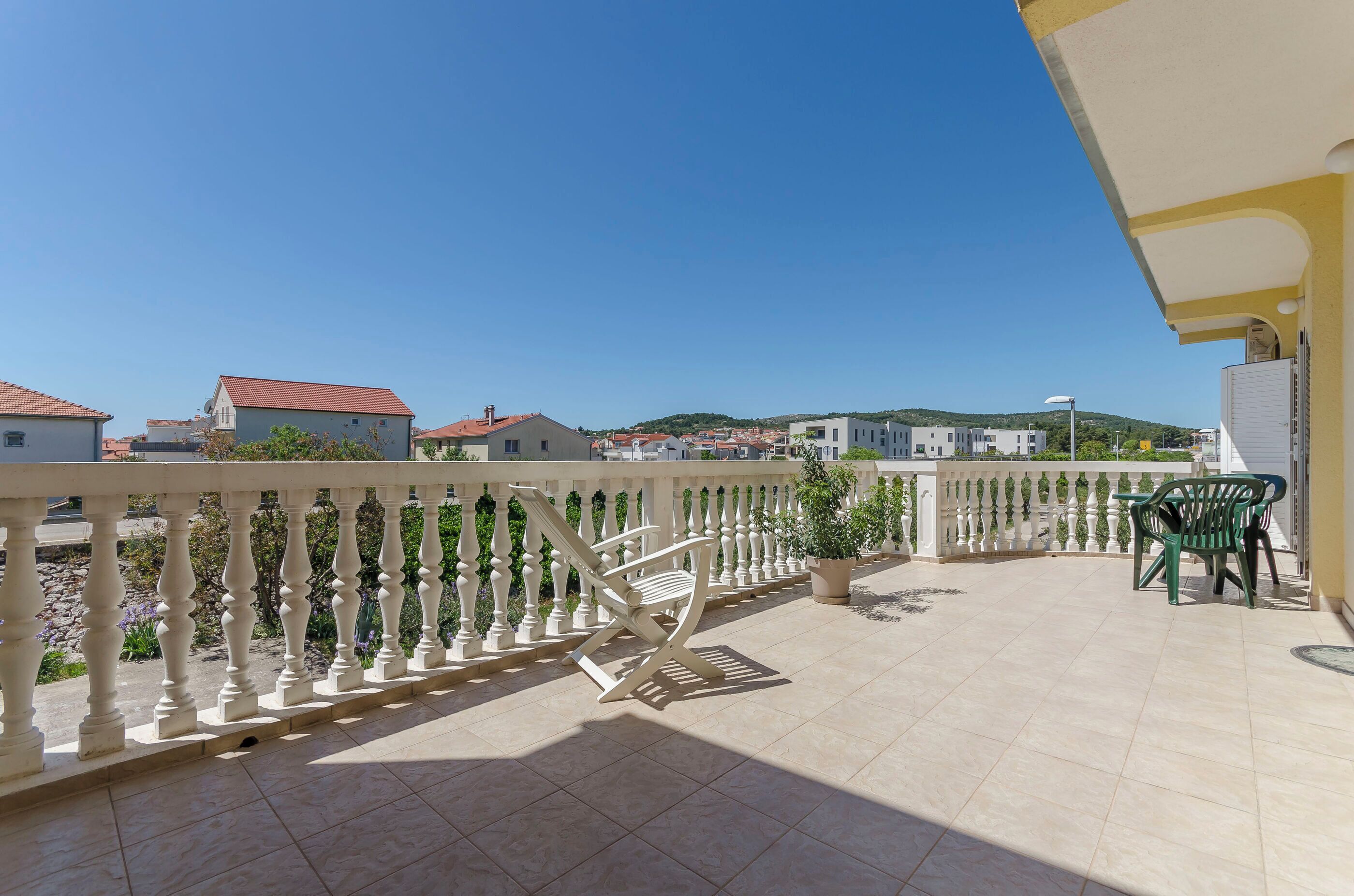 A balcony with a white balustrade, a lounge chair, a table, and a potted plant.