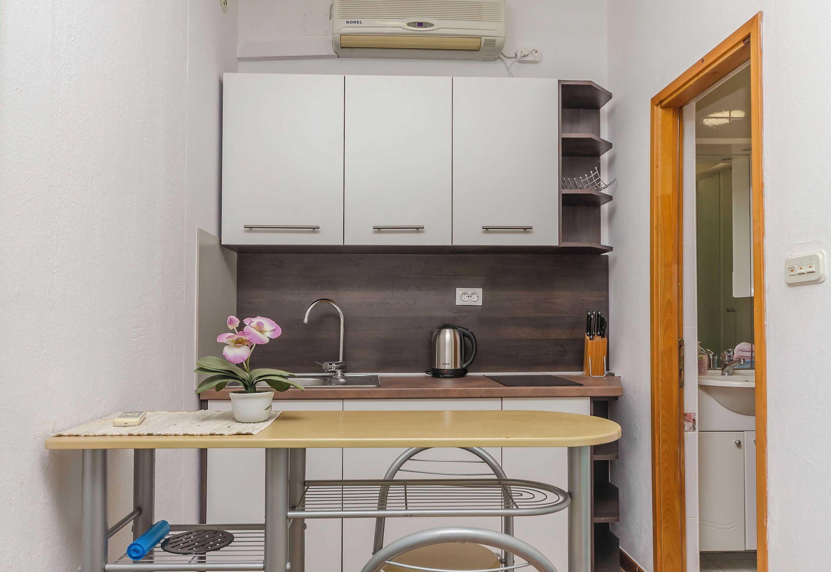 A compact kitchen with white cabinets, a small countertop, a kettle, and a sink.