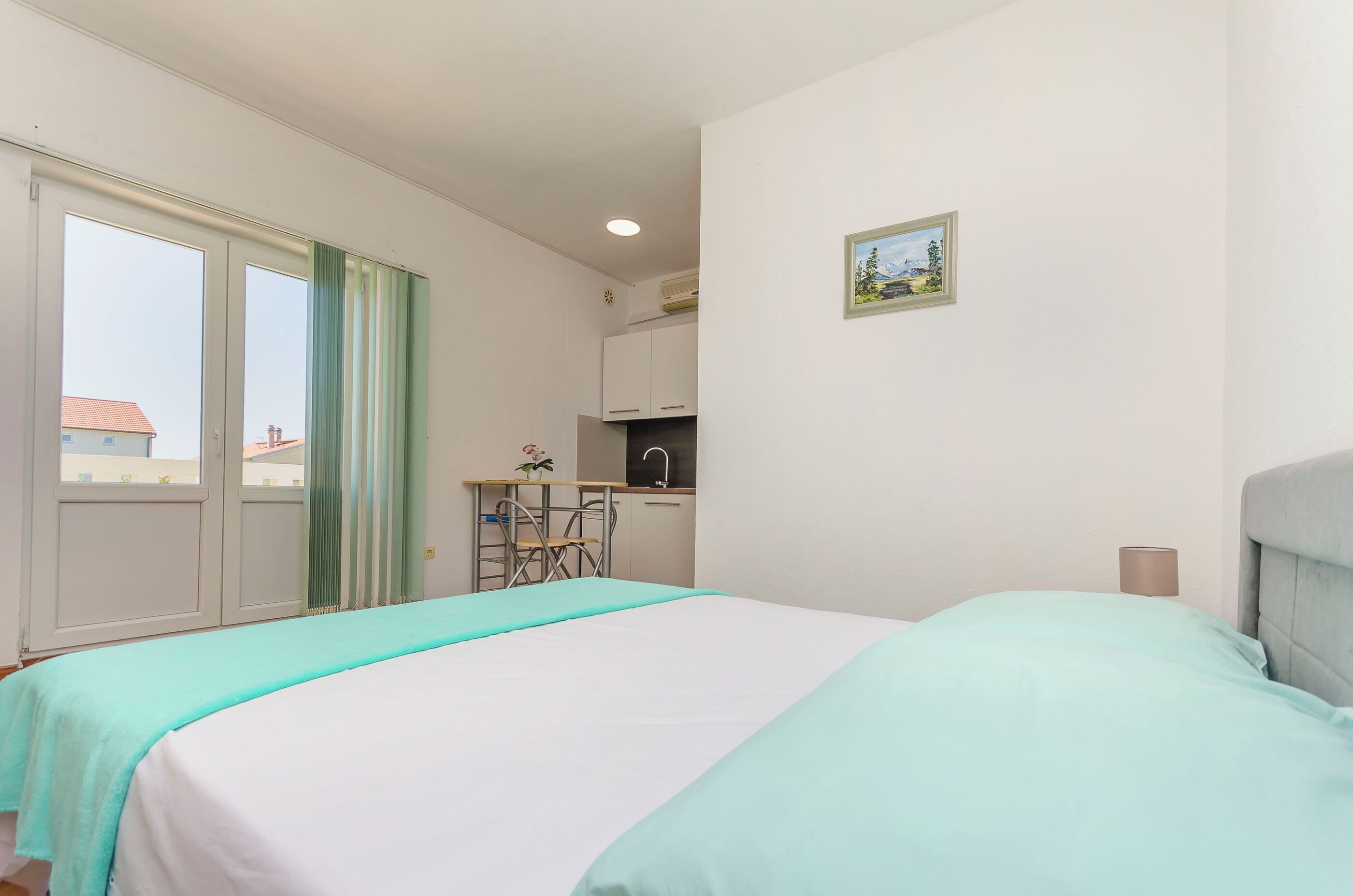 A bedroom with a bed, a small kitchenette, and a window with curtains.