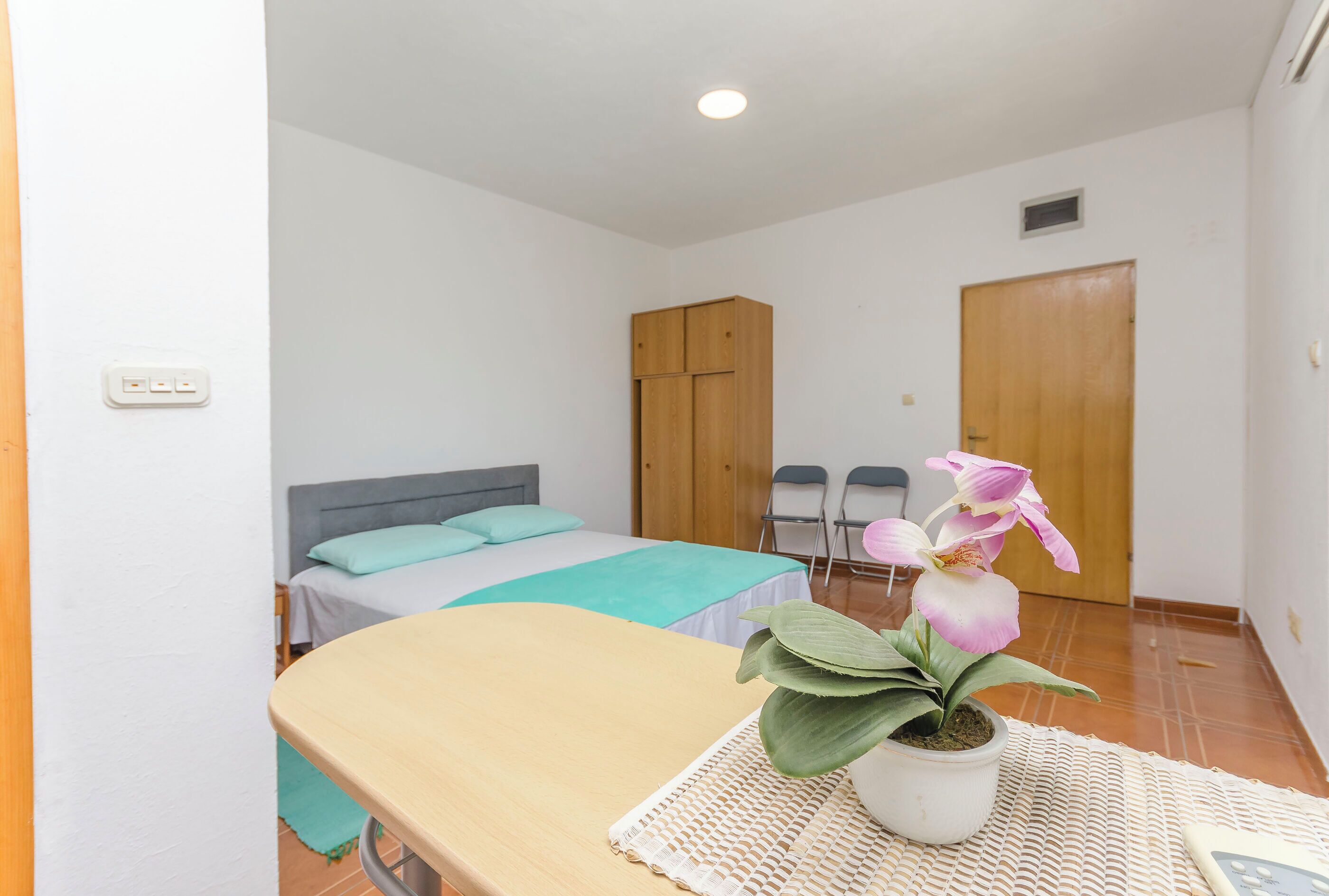 A bedroom with a bed, a desk, a chair, a wardrobe, and a potted plant.