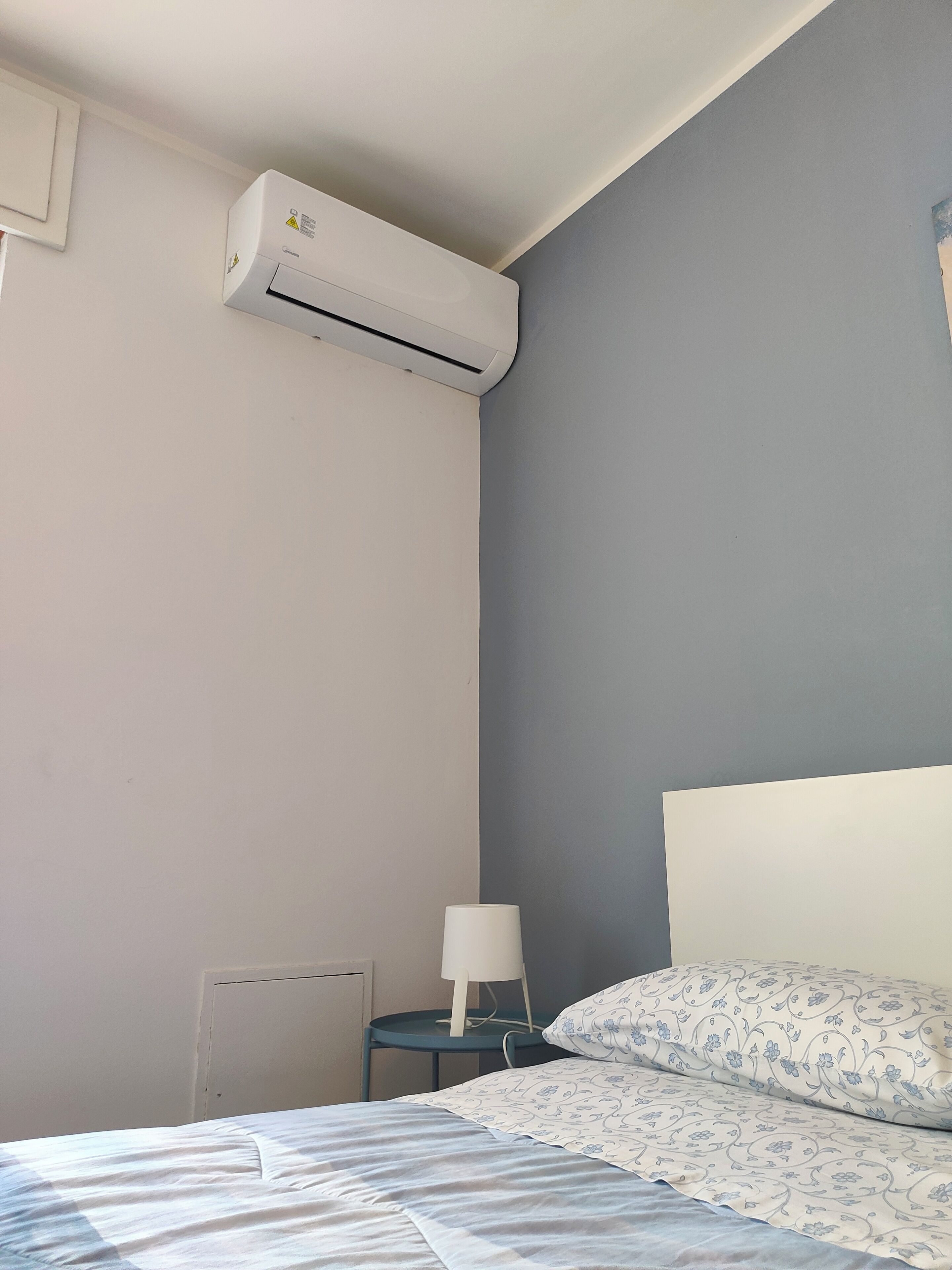 Ein Schlafzimmer mit einem Bett, einem Nachttisch, einer Lampe und einer Klimaanlage.