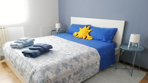 A neatly made bed with blue and white bedding, a bright yellow pillow, and folded towels on the side. - Apartment Ivrea center - UNESCO site (Ivrea)