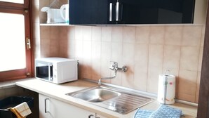 A compact kitchen with a sink, a microwave, and a toaster. There are cabinets above the countertop and a window on the left. - Apartment Ivrea center - UNESCO site (Ivrea)
