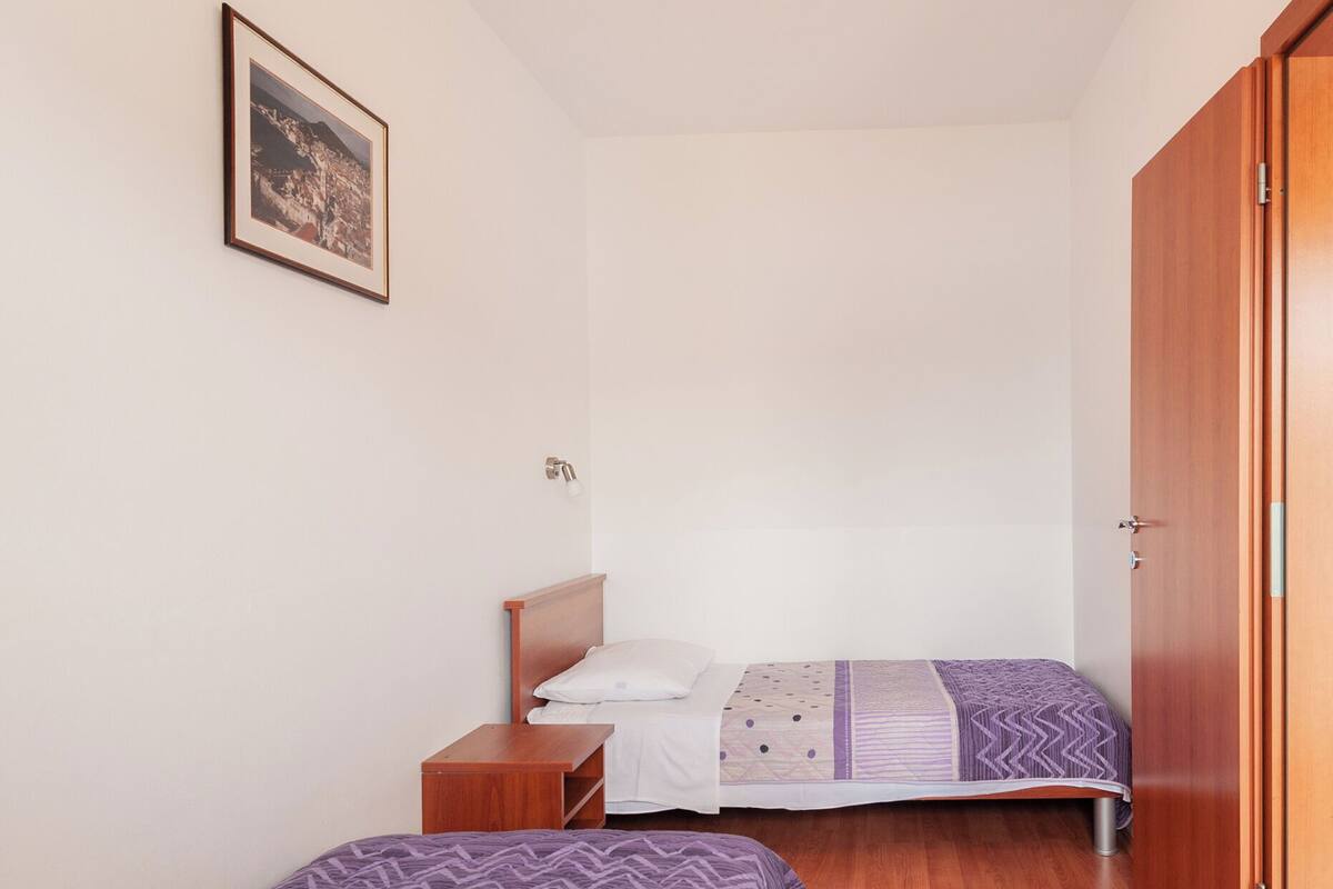 A bedroom with two beds, wooden flooring, a ceiling light, and a door.