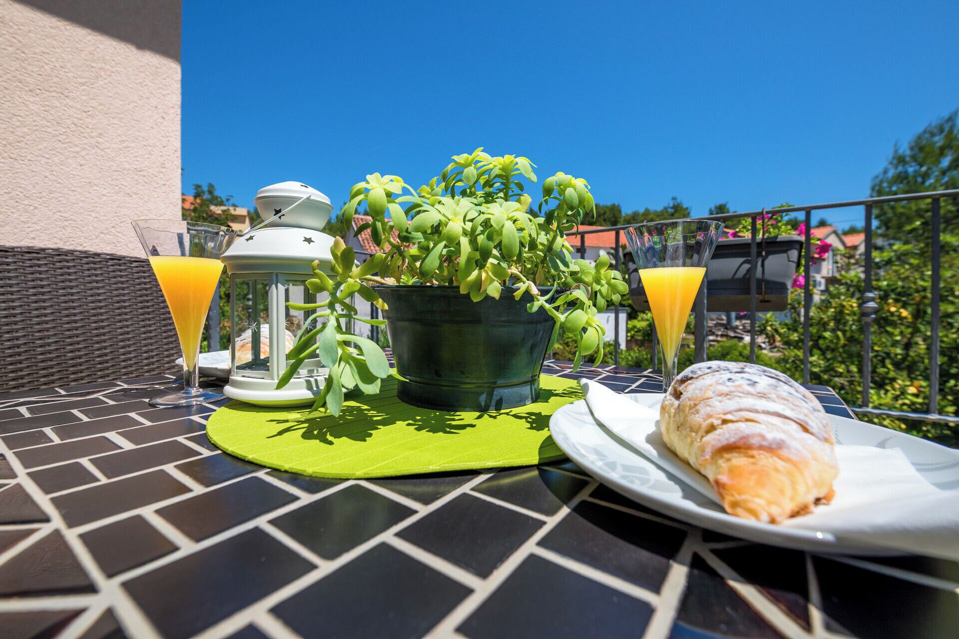 A table with a potted plant, two glasses of orange juice, a lantern, and a plate with a pastry.
