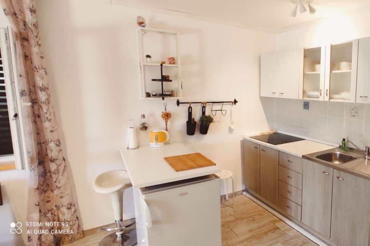A compact kitchen with a sink, cabinets, a small refrigerator, and a clock on the wall.