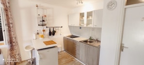 A compact kitchen with a sink, cabinets, a small refrigerator, and a clock on the wall.