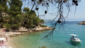 A coastal scene with clear water, a rocky shoreline, and a boat. - Apartments Fran (Vrboska)