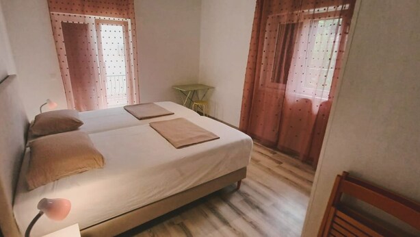 A bedroom with a bed, pillows, a bedside table, and curtains. - Apartments Fran (Vrboska)