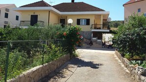 Una casa de dos pisos con balcón, pared de piedra y camino de entrada pavimentado.