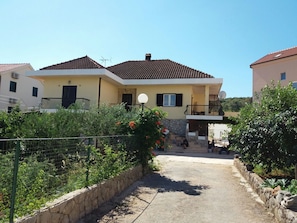 A two-story house with a balcony, a stone wall, and a paved driveway.