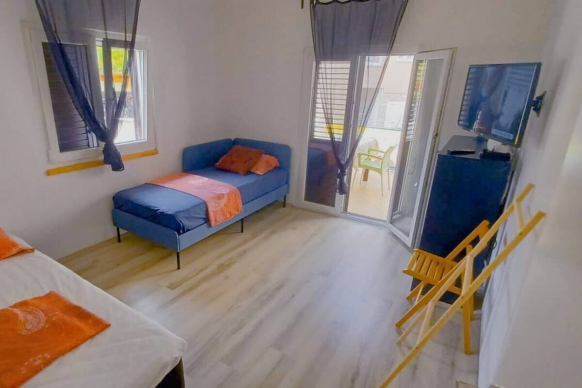 A room with a bed, a sofa, a TV, and a sliding door to an outdoor area.