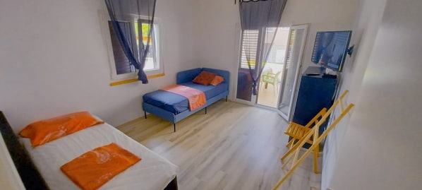 A room with a bed, a sofa, a TV, and a sliding door to an outdoor area.