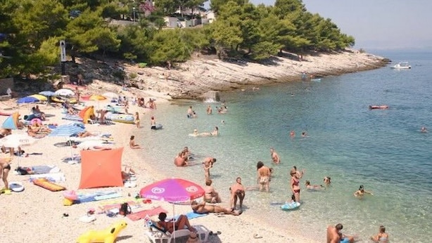 Une plage bondée où les gens se prélassent au soleil et se baignent, avec des parasols et des chaises de plage.