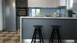 Une cuisine moderne dotée d’un îlot central, de deux tabourets de bar, d’un four encastré et d’un réfrigérateur.