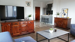 Un salon moderne doté d’un grand téléviseur à écran plat, de meubles en bois, d’un canapé gris et d’une petite table basse agrémentée d’une plante.