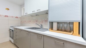 Une cuisine moderne dotée d’un four encastré, d’un évier en acier inoxydable et d’une étagère en bois où sont rangés des verres.