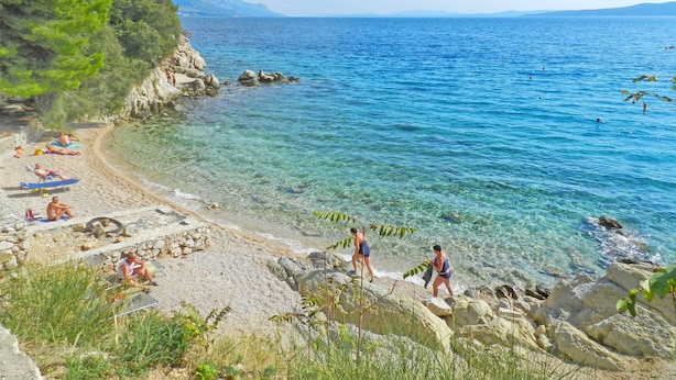 Une plage avec une eau claire, un rivage rocheux et des gens qui prennent un bain de soleil.