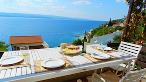 Une table dressée pour deux personnes, avec des assiettes, des verres et une bouteille, donnant sur une vue sur la côte.